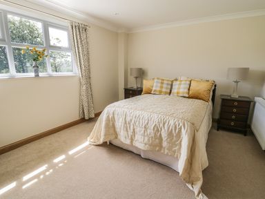 A bedroom with a bed with pillows a window with curtains and a vase with flowers at Rede River Cottage West Woodburn