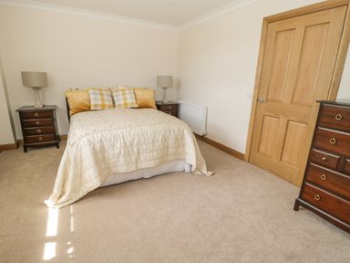 A bedroom with a bed with pillows and two bedside tables with lamps at Rede River Cottage in West Woodburn