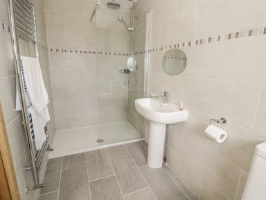 A bathroom with a walk in shower a pedestal sink a towel rack with white towels a round mirror and a toilet paper holder at Rede River Cottage West Woodburn