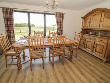A dining room with a wooden table and six wooden chairs near large sliding glass doors at Rede River Cottage in West Woodburn