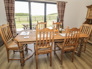 A dining room with wooden table and chairs set for a meal near sliding glass doors with a view of a fenced field at Rede River Cottage in West Woodburn