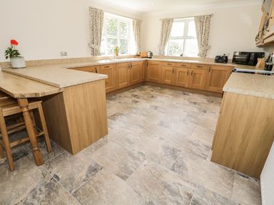 A kitchen with wooden cabinets countertops stools and windows at Rede River Cottage West Woodburn