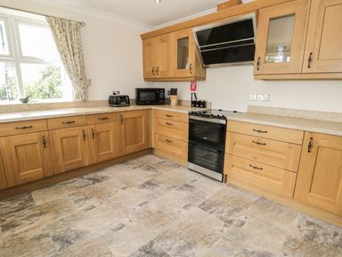 A kitchen with wooden cabinets black appliances and tiled floor at Rede River Cottage in West Woodburn