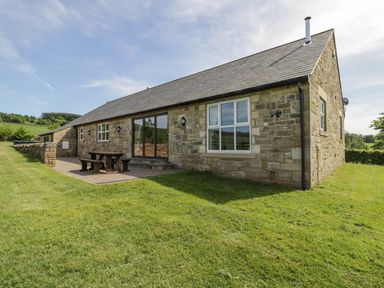 Stone cottage with patio and wooden picnic table on grass at Rede River Cottage in West Woodburn