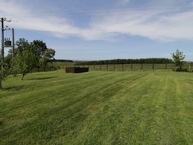 A grassy field with a wooden fence trees and power lines at Rede River Cottage in West Woodburn