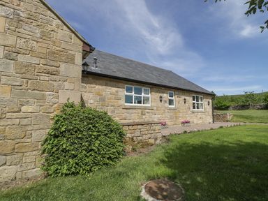 A stone exterior wall of a cottage with windows and green grass at Rede River Cottage in West Woodburn