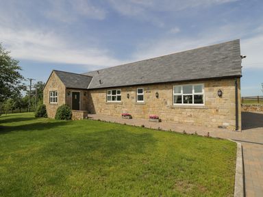 A stone cottage with a slate roof surrounded by grass and a paved driveway at Rede River Cottage in West Woodburn