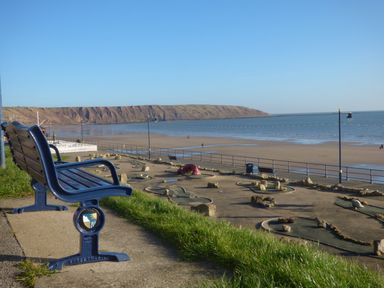 A blue bench overlooking a mini golf course and a beach with cliffs at 104 Sunrise Drive in Filey