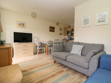 A living room with a gray sofa a television on a dresser and a dining table with chairs at 104 Sunrise Drive in Filey