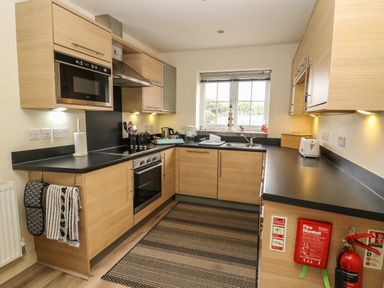A kitchen with wooden cabinets black countertops a microwave an oven a window and a fire extinguisher at 104 Sunrise Drive in Filey