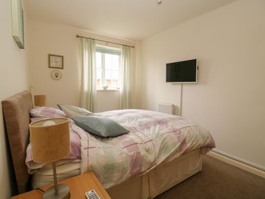 A bedroom with a bed a bedside table lamp a window with curtains and a wall-mounted TV at 104 Sunrise Drive Filey