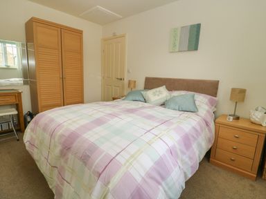 A bedroom with a double bed with pastel checkered bedding a wooden wardrobe a bedside table with a lamp and a desk with a chair at 104 Sunrise Drive Filey