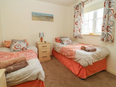 A bedroom with two single beds bedside table lamp and window at 104 Sunrise Drive in Filey