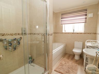 A bathroom with a shower enclosure, bathtub, toilet, sink, and a window with a striped blind at 104 Sunrise Drive in Filey