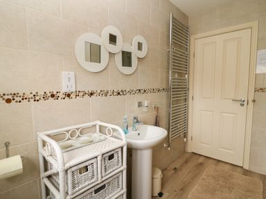 A bathroom with a pedestal sink a wicker storage unit a towel radiator and a closed door at 104 Sunrise Drive in Filey