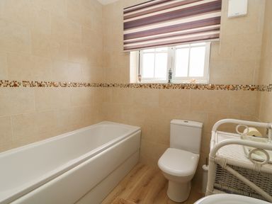 A bathroom with a bathtub a toilet a wicker shelf and a window with striped blinds at 104 Sunrise Drive in Filey