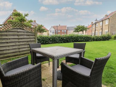 An outdoor seating area with a square table and four chairs on a patio with grass and houses in the background at 104 Sunrise Drive Filey