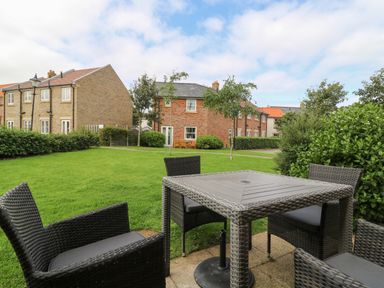 An outdoor patio area with a table and four chairs on a lawn near residential buildings at 104 Sunrise Drive in Filey