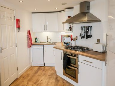 A kitchen with white cabinets wooden countertop a gas stove oven sink dishwasher and various utensils at 10 Oceanside in Ilfracombe