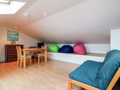 A room with a wooden dining table and chairs a chest of drawers bean bags and a futon at 10 Oceanside in Ilfracombe