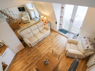 A living room with white leather sofas a wooden dining table and chairs wooden flooring and glass doors at 10 Oceanside in Ilfracombe