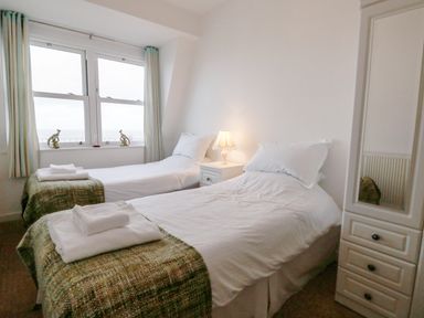 A bedroom with two single beds bedside table with lamp wardrobe with mirror 10 Oceanside in Ilfracombe