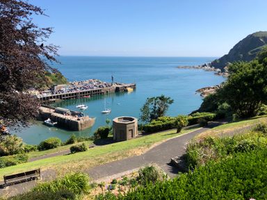 A coastal bay with boats docked near a pier and a pathway with greenery overlooking the sea at 10 Oceanside in Ilfracombe