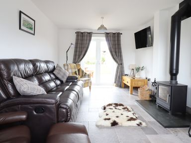 A living room with a leather sofa armchair wood stove and TV at Gwynfa in Rhyd Uchaf near Bala Gwynedd