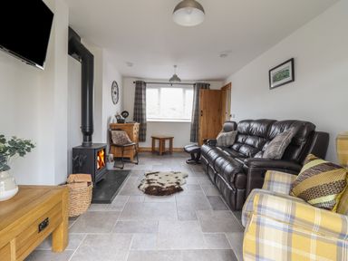A living room with a brown leather sofa a yellow plaid armchair a wood burning stove and a wooden table at Gwynfa in Rhyd Uchaf near Bala Gwynedd