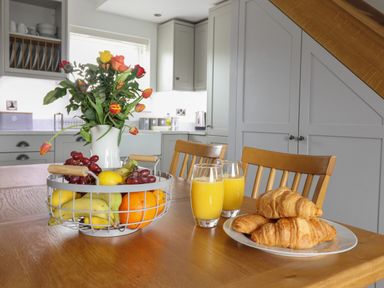 A kitchen with a wooden table holding a basket of fruit a vase with flowers two glasses of orange juice and a plate of croissants at Gwynfa in Rhyd Uchaf near Bala Gwynedd