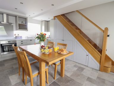 A kitchen with a wooden dining table and chairs next to stairs and gray cabinets at Gwynfa in Rhyd Uchaf near Bala Gwynedd