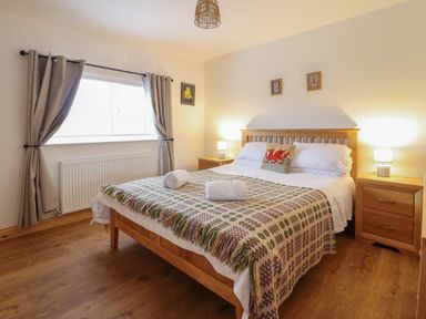 A bedroom with a wooden bed and bedside tables with lamps and a window with curtains at Gwynfa in Rhyd Uchaf near Bala Gwynedd