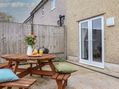 A wooden picnic table with cushions flowers croissants and orange juice near a house with glass doors at Gwynfa in Rhyd Uchaf near Bala Gwynedd
