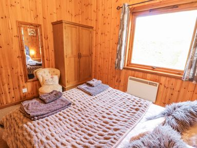 A bedroom with a bed, wardrobe, mirror, and chair at 26 Dukes Meadow in Greystoke near Penrith