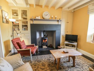 A living room with a fireplace armchairs a wooden coffee table television and built in cupboards at Miners Cottage in Blaenau Ffestiniog