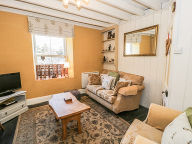 A living room with patterned sofas wooden coffee table a rug television and a window at Miners Cottage in Blaenau Ffestiniog