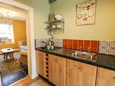 A kitchen with wooden cabinets a sink and shelves next to a room with a couch and wooden table at Miners Cottage in Blaenau Ffestiniog
