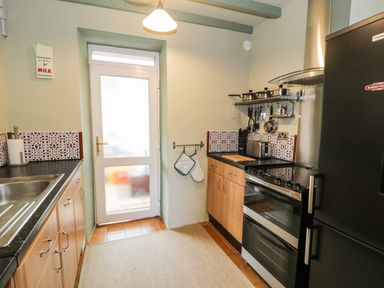 A kitchen with wooden cabinets a black refrigerator a stove a sink and a door at Miners Cottage in Blaenau Ffestiniog