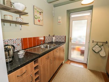 A kitchen with wooden cabinets a sink a door and kitchen utensils at Miners Cottage in Blaenau Ffestiniog