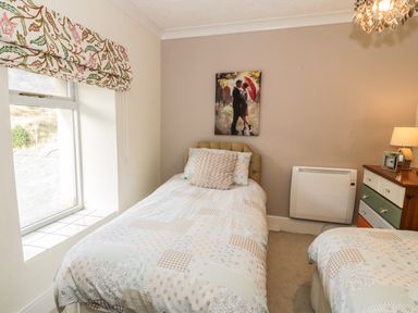 A bedroom with two single beds a window with patterned curtains a chest of drawers and a painting on the wall at Miners Cottage in Blaenau Ffestiniog