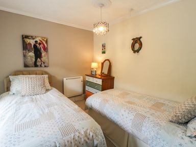 A bedroom with two single beds a chest of drawers with a lamp and mirror and wall decorations at Miners Cottage in Blaenau Ffestiniog