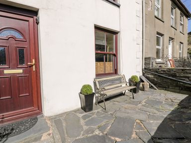A stone patio with a wooden bench and two potted plants outside a house with a red door at Miners Cottage in Blaenau Ffestiniog