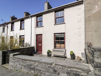 A white terraced house with red doors and windows and a stone wall in front at Miners Cottage in Blaenau Ffestiniog