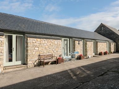 A stone building with light green doors brown bench blue table and chairs and flower pots outside at Snowdrop Cottage in Llantwit Major