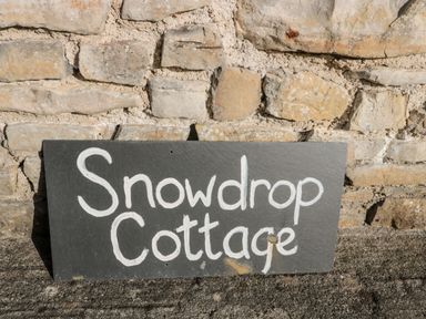 A stone wall with a black rectangular sign reading Snowdrop Cottage in white letters at Snowdrop Cottage in Llantwit Major