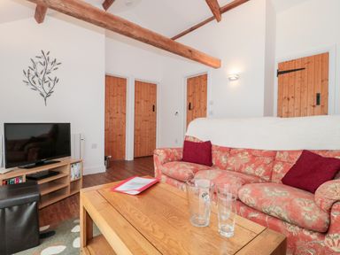 A living room with a floral sofa red cushions wooden beams three wooden doors and a wooden coffee table with glassware at Snowdrop Cottage in Llantwit Major