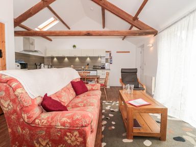 A living area with red floral sofa, wooden coffee table, black armchair, dining table, and kitchen cabinets at Snowdrop Cottage in Llantwit Major