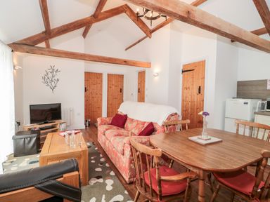 A living and dining area with wooden beams a floral sofa wooden dining table and doors at Snowdrop Cottage in Llantwit Major