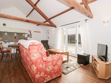 A living room with wooden beams a red floral sofa a wooden coffee table and kitchen area at Snowdrop Cottage in Llantwit Major