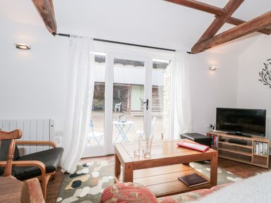 A living room with wooden beams a coffee table television and glass doors opening to an outdoor seating area at Snowdrop Cottage in Llantwit Major